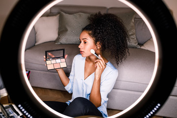 Woman beauty vlogger recording a makeup tutorial on camera using ring light - obrazy, fototapety, plakaty
