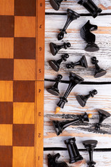 Chess pieces lying next to chess board. Black chess figures lying on wooden background, top view. Way to improve your brain fitness.