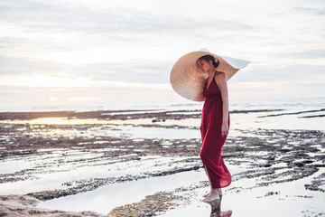 Elegant lady in straw hat and red dress on beach