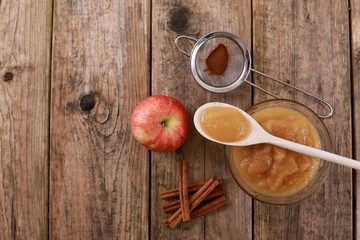 fresh homemade apple jam, apple puree with cinnamon in a bowl with wooden spoon and apples on wooden rustic table