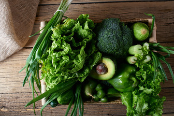 Green vegetables and fruits and greens in a brown wicker basket on a wooden background. Healthy eating concept