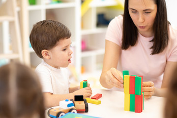 Teacher and kids playing together with colorful toys building blocks in preschool