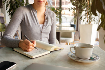 The girl takes notes in a notebook, next to a laptop and phone