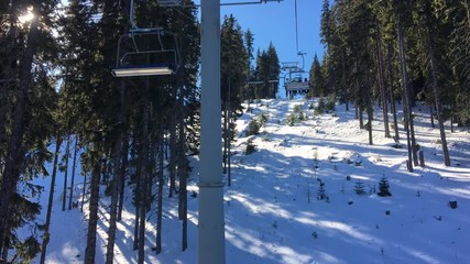 4K video clip of four person ski chair lift going through the trees up a mountain with a blue sky