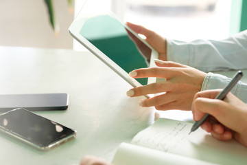 The girl touches the tablet screen with her finger, the second girl takes notes in the black