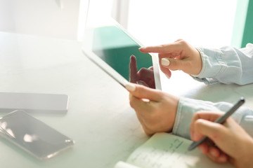 The girl touches the tablet screen with her finger, the second girl takes notes in the black
