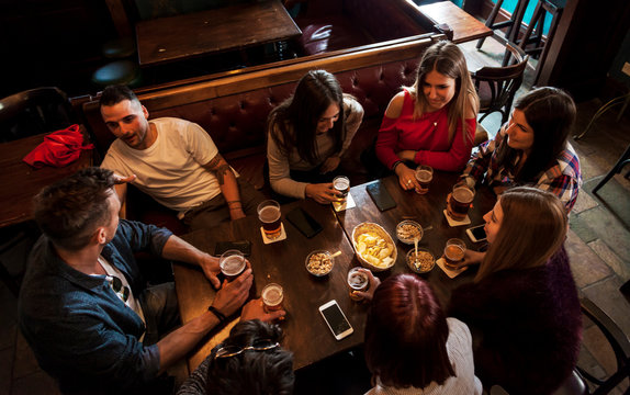 group of millennials people celebrating in a pub drinking beer