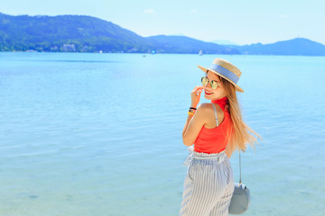 stylish young woman smiles near lake and mountains on travel vac