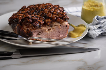 Deutscher Krustenbraten aus Schweinefleisch mit Senf auf Teller mit Küchenmesser und Fleischgabel auf Marmor Hintergrund