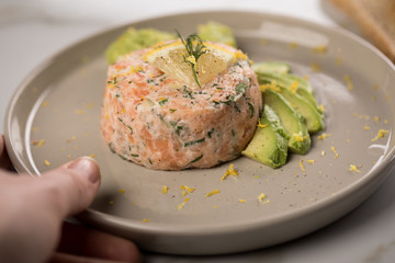 Frau isst rohes Lachstatar mit Lachs, Dill, Zitrone, Avocado und Vollkorn Toast Brot auf Porzellan Teller und Marmor Hintergrund