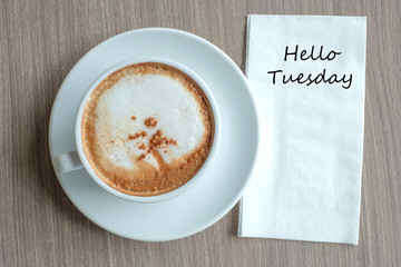 Hello Tuesdy text on paper with hot cappuccino coffee cup on table background at the morning