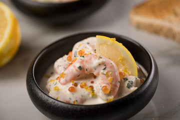 Garnelen Salat mit Lachs Kaviar,  Kräuter, Zitrone, und Vollkorn Toast Brot in schwarzer Schale auf Marmor Hintergrund