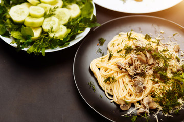 Close-up of delicious pasta with mushrooms and greens in a plate on a black background