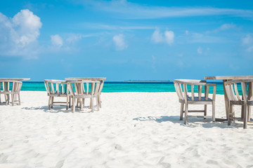 Chairs and Tables on the white beach at the maldives with the turqoise ocean in the background and clouds on the blue sky