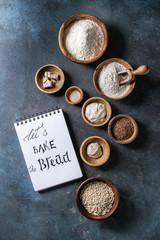 Ingredients for baking bread. Variety of wheat and rye flour, grains, yeast, sourdough and notebook with handwritten lettering over dark blue texture background. Flat lay, space