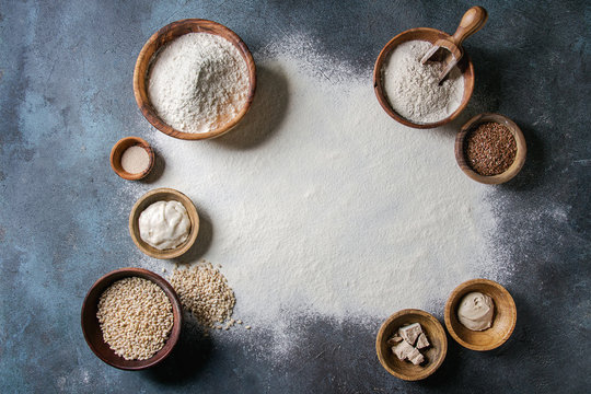Ingredients for baking bread. Variety of wheat and rye flour, grains, yeast, sourdough and sifted flour over dark blue texture background. Flat lay, space