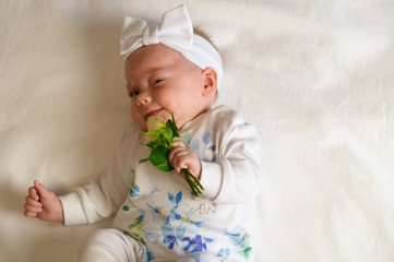 Beautiful baby girl holding a flower on white blanket