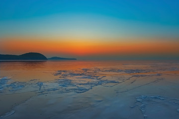 Obraz premium Seascape with bright orange sunset and ice floes at the coastline.