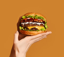 Woman hands hold big double cheeseburger burger sandwich with beef and bacon on yellow - obrazy, fototapety, plakaty