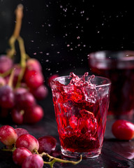 A glass of fresh grape juice, grape juice canning. Dark background, splashes and drops in a glass.