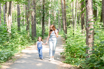 Fototapeta premium Family, nature and people concept - Mom and daughter spend time together on a walk in the green park