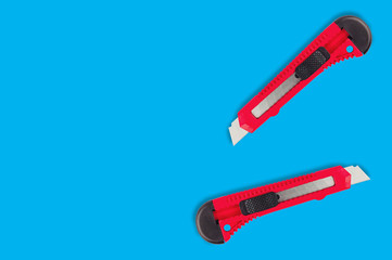 Pair of stationery knives with red plastic handle on blue background with copy space for your text