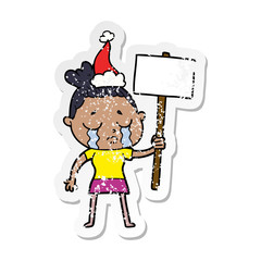 distressed sticker cartoon of a crying woman with protest sign wearing santa hat