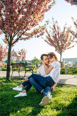 Fototapeta premium Couple hugs near sakura trees in blooming garden. Couple in love spend time in spring garden, flowers on background, close up. Passion and love concept.