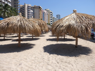 Tropical bamboo umbrellas on sandy beach at bay of ACAPULCO city in Mexico with hotel buildings