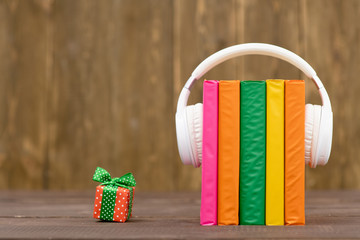 Plakat Multicolored books with white headphones and gift box on wooden background. Empty space for text