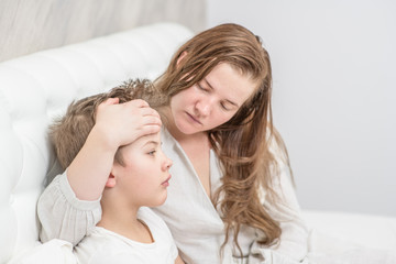Mother with sick boy on the bed touches his forehead, checking the temperature