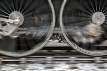 The rotating wheels of steam locomotive on railroad. Detail of steam locomotive wheel on tracks.