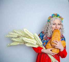 charming chubby smiling girl with big ears of ripe wheat and fresh bread in her hands. woman dressed in a traditional rustic costume and stands on white solid background in the Studio.