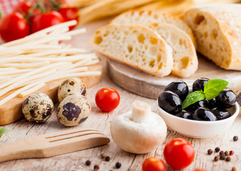 Homemade wheat bread with quail eggs and raw wheat and fresh tomatoes on wooden background. Classic italian village food. Garlic, black and green olives. Wooden spatula