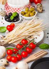 Homemade spaghetti pasta with quail eggs with bottle of tomato sauce and cheese on kitchen background. Classic italian village food. Garlic, champignons, black and green olives, pan and spatula.