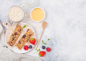 Organic cereal granola bar with berries on round vintage board with honey spoon and jar of oats on marble background. Strawberry, raspberry and blueberry with mint leaf and bowl of honey