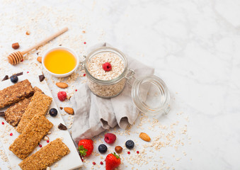 Organic cereal granola bar with berries on marble board with honey spoon and jar of oats and linen towel on marble background. Space for text.Top view