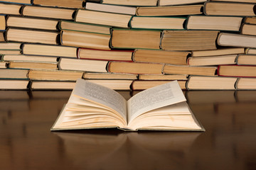 Open book on the desk with background of book piles