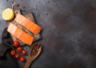 Fresh raw salmon slice on chopping board with pepper tomatoes and lemon on stone kitchen table background. Space for text. With rosemary and salt