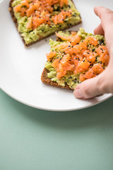 Frau isst Avocado Räucherlachs Vollkorn Sonnenblumenkern Brot und Sesam zum Frühstück auf grünen Hintergrund
