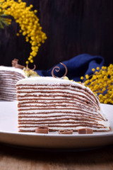 Piece of chocolate crepes cake with cream cheese on a white plate