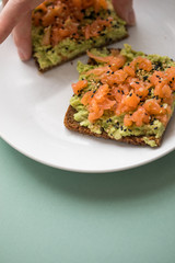 Frau isst Avocado Räucherlachs Vollkorn Sonnenblumenkern Brot und Sesam zum Frühstück auf grünen Hintergrund