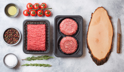 Tray with raw minced homemade beef meat with spices and herbs. Top view. On top of kitchen table background. With chopping board and knife and raw burgers.
