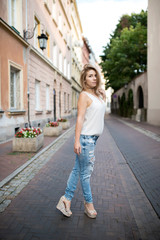 Portrait of beautiful young adult woman standing on street in old town. Posing in white shirt and jeans.