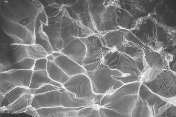 Black and white water surface with bright sun light reflections, water in swimming pool background