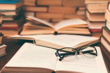Fototapeta premium Open book and glasses on wood desk in the library room with blurred focus for education background and back to school concept