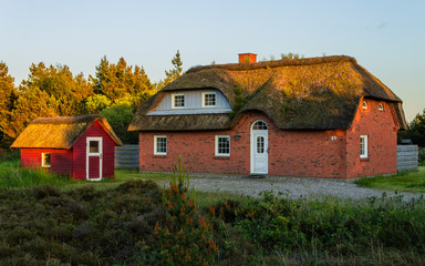 Fototapeta na wymiar Panoramic view of a traditionally brick built house, thatched roof and small cottage. Beautiful Scene of holiday home in the near of the north sea during sunset. Romo, Tonder, Denmark, Europe
