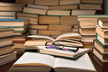 Open books and glasses on wood desk in the library room with blurred focus for education background and back to school concept