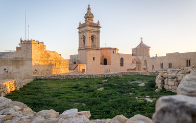 Detail view on the old, historical St. Joseph's Chapel inside the Citadel of Victoria inside antique ruins walls with grass field and sandstones in the foreground on Gozo, Malta