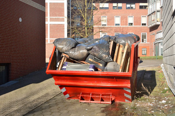 Full orange metal Skip container standing on the road near the house. In the container are old...